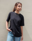 Woman wearing a black t-shirt and light blue jeans against a beige wall