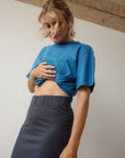 Woman wearing a blue top and dark skirt against a plain background