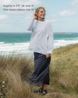 Woman standing on a grassy hill by the ocean wearing a striped t-shirt and dark skirt.