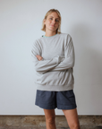 Person wearing a grey sweater and dark shorts against a plain background
