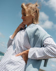 Woman wearing a light blue sweatshirt over a striped t-shirt with a clear sky background