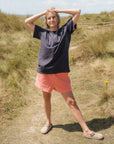 Person wearing a black t-shirt and pink shorts standing in a grassy field.