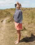 Woman in a Breton striped tee shirt and pink shorts standing on a grassy path with a clear sky.