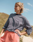 Woman wearing a navy blue and white t-striped shirt with pink sweat shorts standing outdoors against a blue sky.