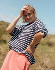Woman wearing a navy blue and white striped t-shirt and pink shorts standing in a grassy field.