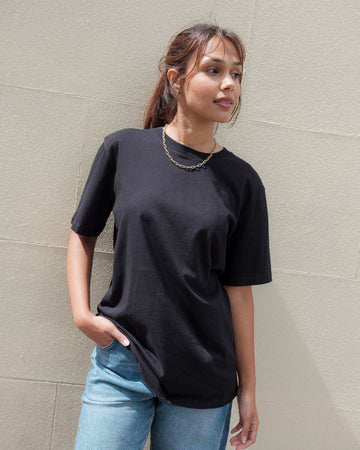 Woman wearing a black t-shirt and light blue jeans against a beige wall