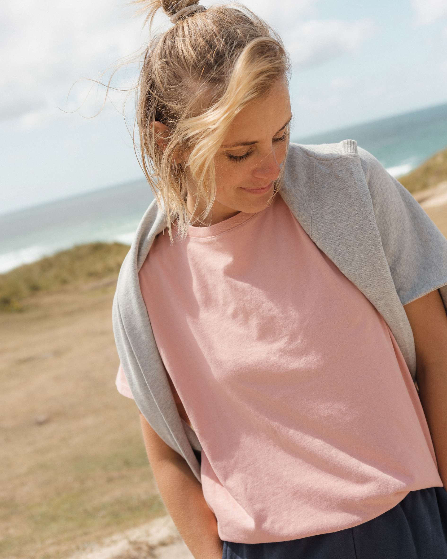 Woman wearing a pink shirt and grey sweatshirt on a beach