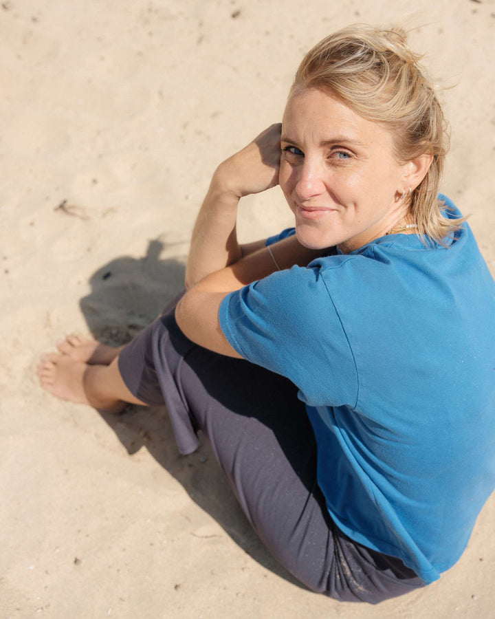 Person sitting on sand wearing a blue shirt and gray pants