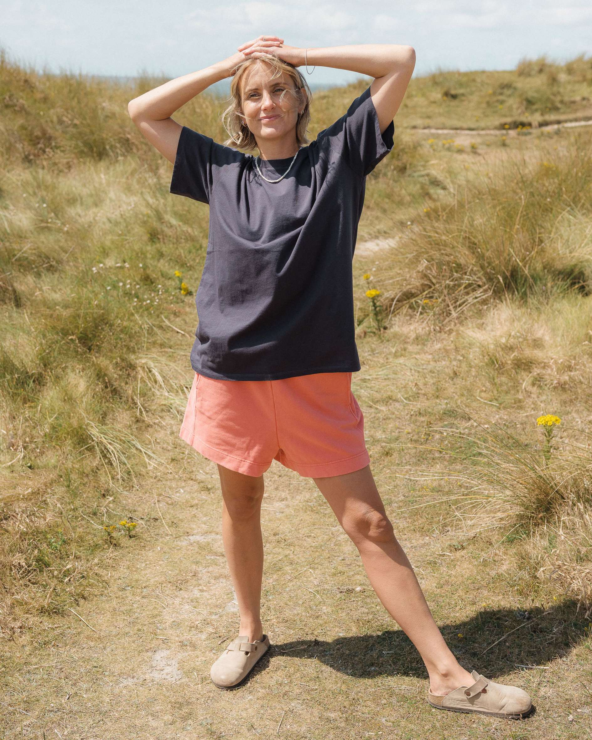 Person wearing a black t-shirt and pink shorts standing in a grassy field.