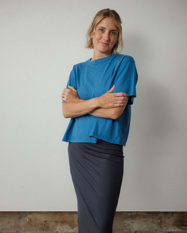 Woman wearing a blue top and dark skirt against a plain background