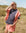 Woman in a coral outfit standing in a grassy field with a clear sky.